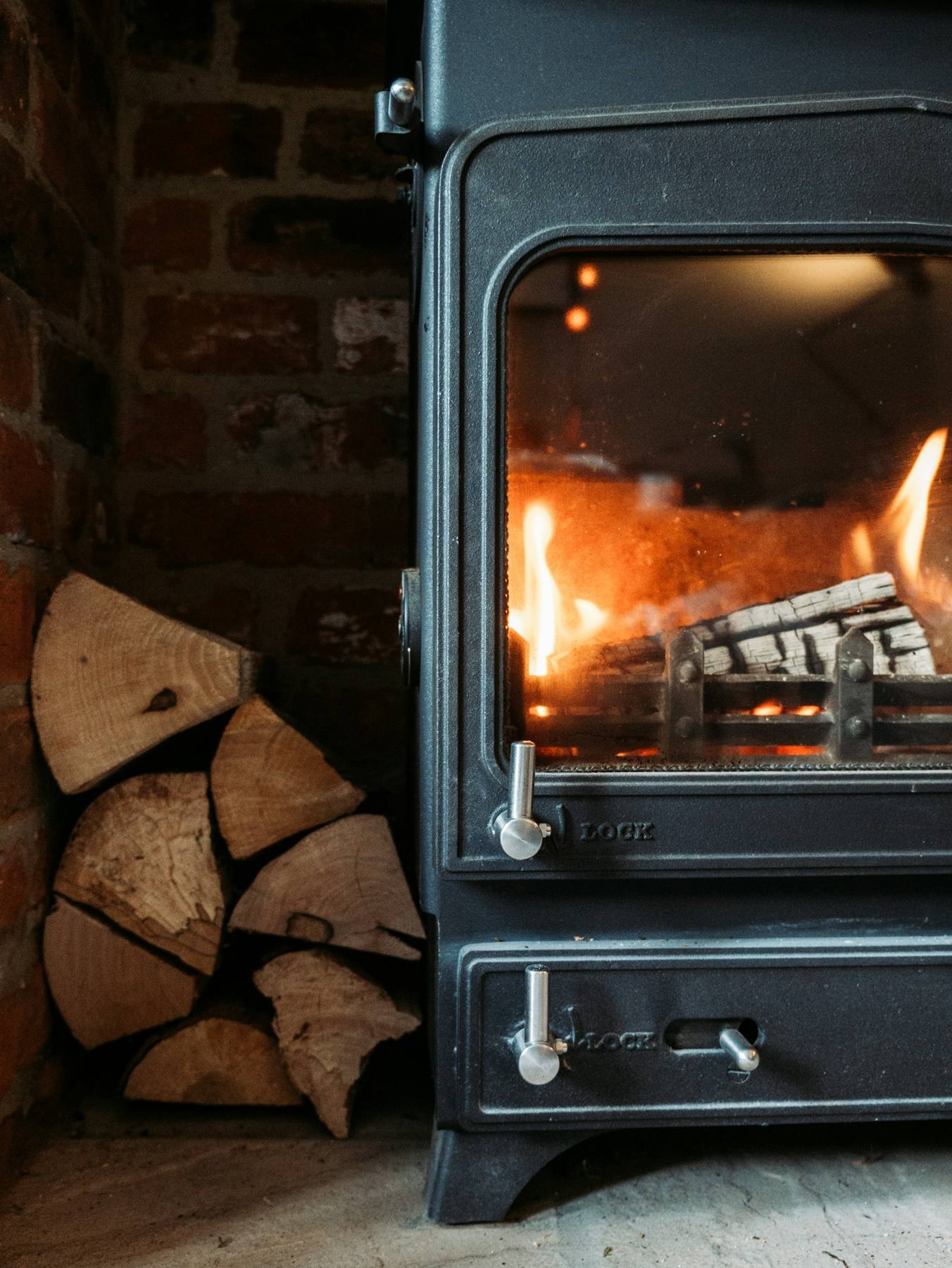 A black wood-burning stove with a glowing fire beside neatly stacked kiln-dried logs